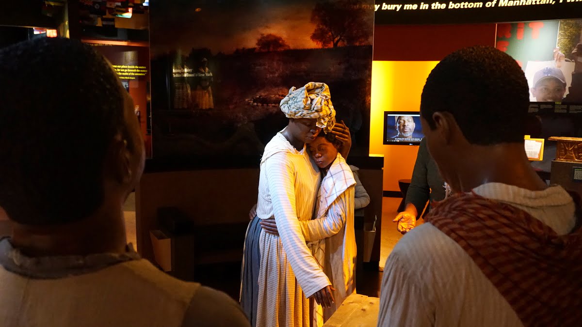 Picture of the African Burial Ground National Monument Wax figures, with a mom and child in the center and further from the camera, with two adult men with heads to the back of the camera and closer to the camera. National Parks in New York City - New York Weekend Trip Travel Guide | Sincerely Yasmin