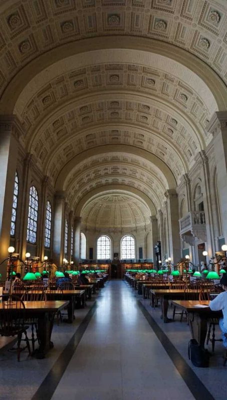 Picture of the interior of the Boston Public Library Main Reading Room. Vaulted detailed ceilings and rows of long wooden tables with green lamps on them. | The Yasmin Diaries