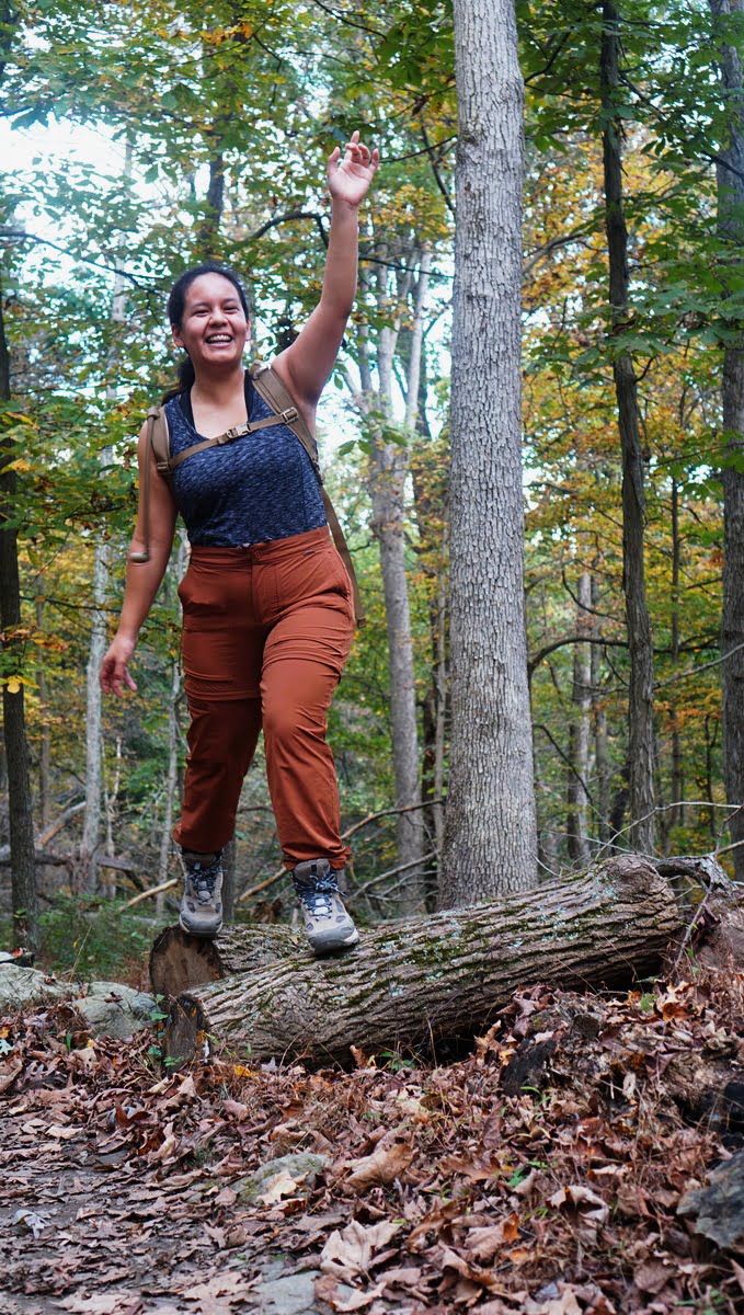 Yasmin jumping on logs while wearing a gray sports tank top and burnt orange hiking pants - REI Hiking Pants Review | Convertible Hiking Pants for Petite Women | Sincerely Yasmin